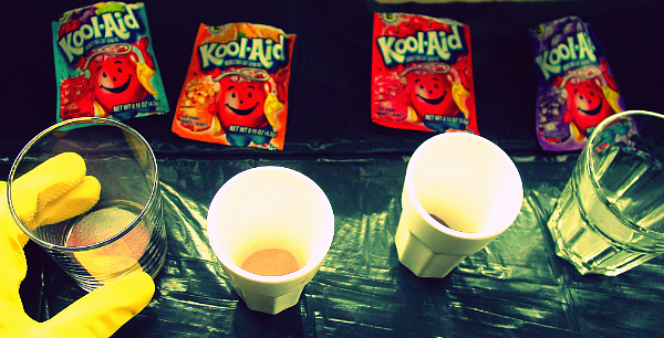 Kool-Aid and cups Rubber-gloved hand, four Kool-Aid packets, and some cups