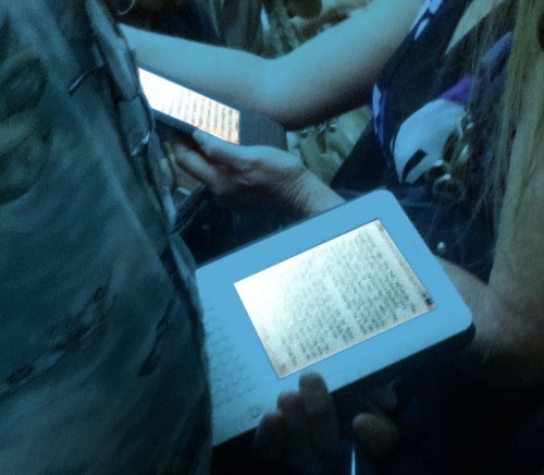 Kindle-reading couple riding the NYC subway; one screen shows large type, the other small